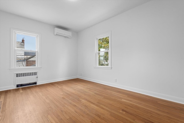 spare room featuring light wood-style floors, radiator, a wall mounted air conditioner, and baseboards