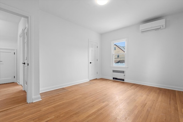 spare room with radiator, light wood-style flooring, baseboards, and a wall mounted AC