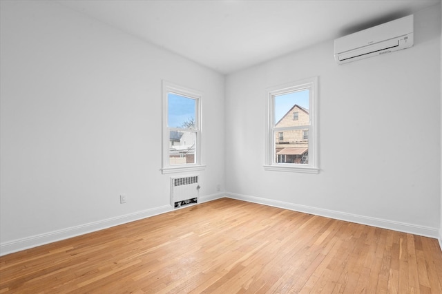 spare room with light wood-type flooring, a healthy amount of sunlight, a wall unit AC, and radiator