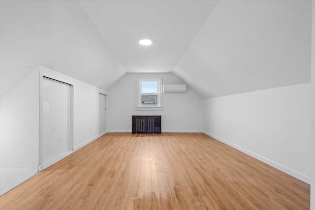 additional living space featuring radiator, light wood-style floors, vaulted ceiling, a wall mounted air conditioner, and baseboards