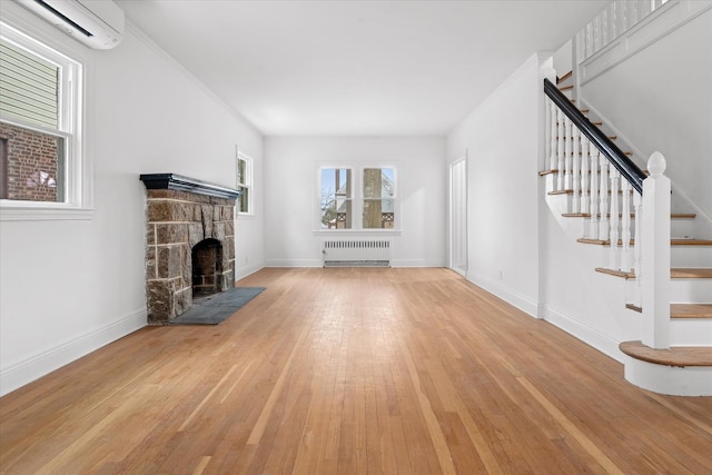 53-31 212th St, Bayside, NY 11364 - unfurnished living room with radiator heating unit, a wall mounted AC, a stone fireplace, light wood-type flooring, and stairs