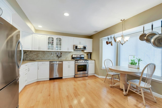 kitchen with glass insert cabinets, light stone countertops, stainless steel appliances, light wood-style floors, and backsplash