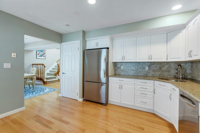 kitchen featuring light stone countertops, stainless steel appliances, light wood-style floors, white cabinetry, and a sink