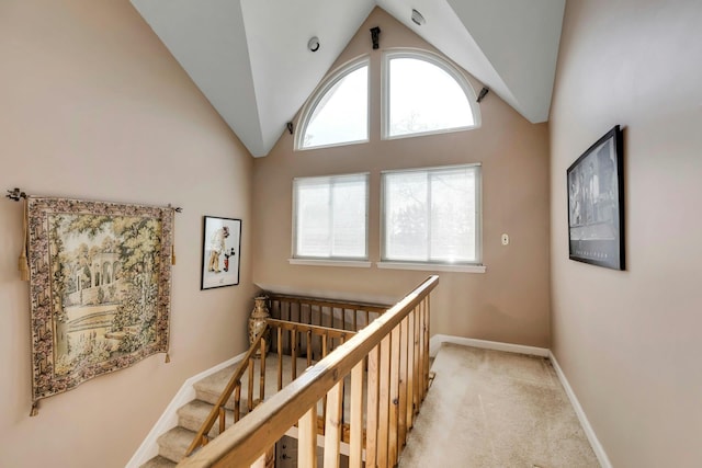 hall featuring light carpet, high vaulted ceiling, baseboards, and a wealth of natural light