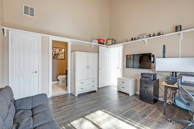 office space featuring dark wood-type flooring, a high ceiling, and visible vents