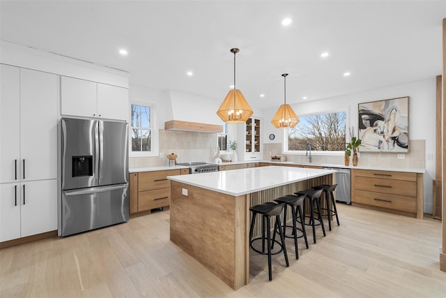 kitchen featuring plenty of natural light, custom range hood, appliances with stainless steel finishes, a kitchen bar, and a sink