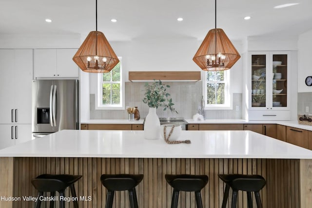 kitchen with a notable chandelier, white cabinetry, light countertops, stainless steel refrigerator with ice dispenser, and decorative backsplash