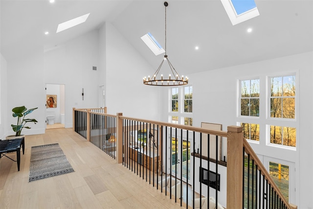 hallway featuring a skylight, a notable chandelier, an upstairs landing, wood finished floors, and high vaulted ceiling