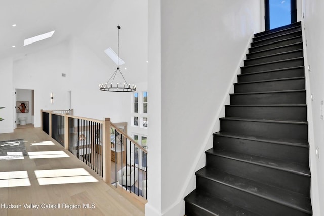 stairway featuring a skylight, high vaulted ceiling, a notable chandelier, and wood finished floors