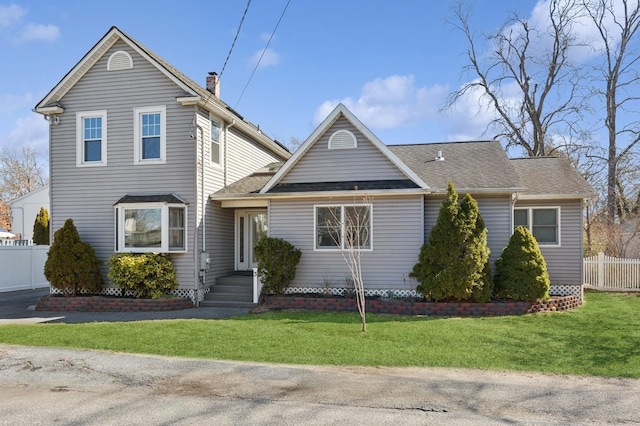 traditional-style house featuring a shingled roof, a chimney, a front lawn, and fence