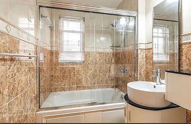 full bath with shower / bath combination with glass door, plenty of natural light, tile walls, and vanity