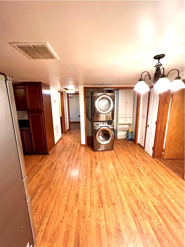 corridor with stacked washer and dryer, light wood finished floors, and visible vents