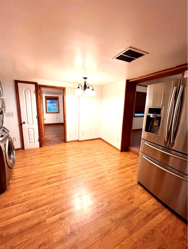 kitchen with light wood-style flooring, visible vents, stainless steel refrigerator with ice dispenser, and stacked washer and clothes dryer