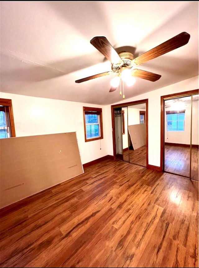 unfurnished bedroom featuring ceiling fan, wood finished floors, two closets, and baseboards