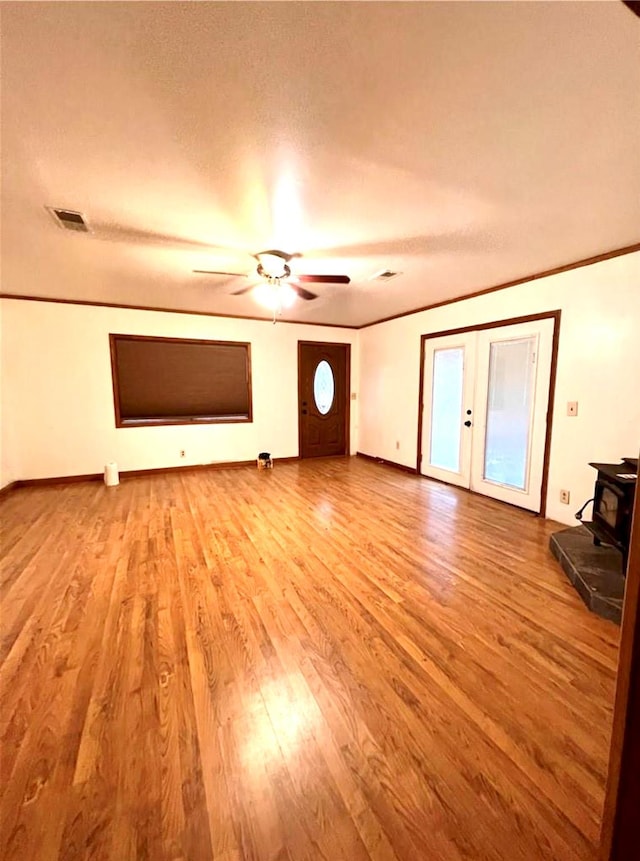 unfurnished living room with french doors, visible vents, ornamental molding, a wood stove, and wood finished floors