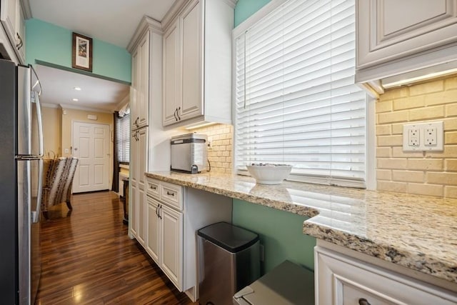 kitchen featuring tasteful backsplash, light stone counters, ornamental molding, dark wood-style flooring, and freestanding refrigerator