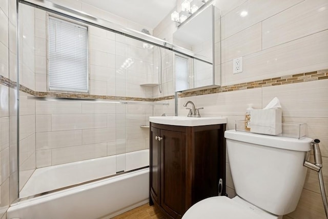 full bathroom featuring combined bath / shower with glass door, tile walls, toilet, and vanity