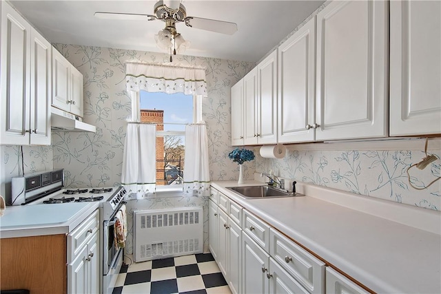 kitchen with light floors, white gas range, radiator heating unit, under cabinet range hood, and wallpapered walls