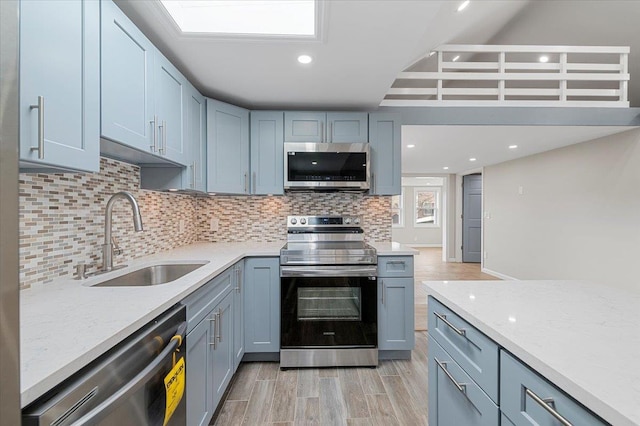 kitchen with light stone counters, decorative backsplash, appliances with stainless steel finishes, a sink, and light wood-type flooring