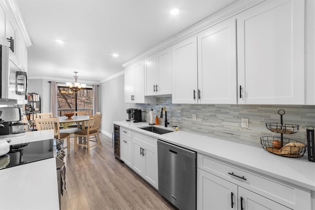 kitchen featuring a sink, stainless steel appliances, crown molding, a chandelier, and white cabinets