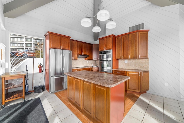 kitchen with visible vents, under cabinet range hood, appliances with stainless steel finishes, a kitchen island, and tasteful backsplash