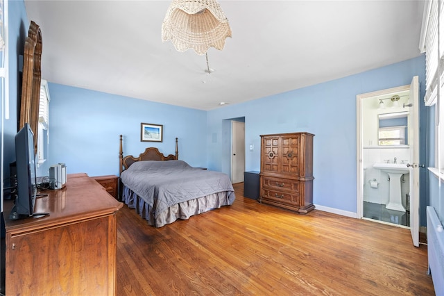 bedroom with ensuite bath, a notable chandelier, wood finished floors, and baseboards