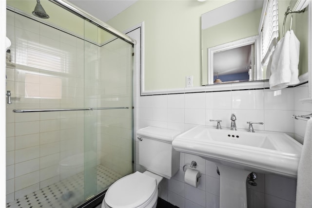 bathroom with tile walls, toilet, a stall shower, and a sink