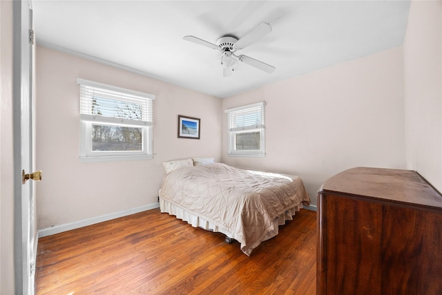 bedroom with a ceiling fan, multiple windows, wood finished floors, and baseboards