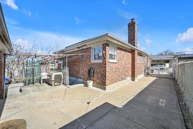 view of property exterior featuring a patio, brick siding, fence, a gate, and a chimney