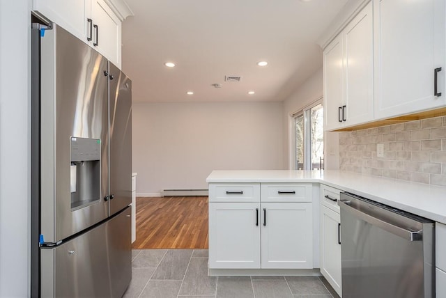 kitchen with light countertops, decorative backsplash, appliances with stainless steel finishes, a peninsula, and a baseboard radiator