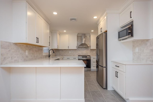 kitchen with visible vents, wall chimney range hood, stainless steel appliances, a peninsula, and light countertops