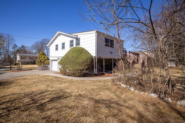 view of property exterior with stairway, driveway, an attached garage, and a yard