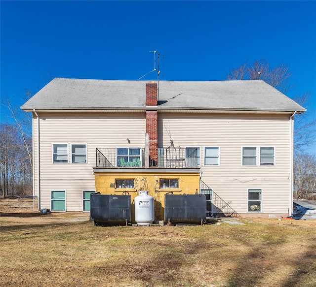 rear view of property with a lawn, heating fuel, and a balcony