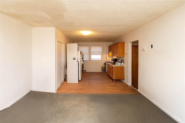 kitchen featuring brown cabinets, light carpet, gas range gas stove, light countertops, and baseboards