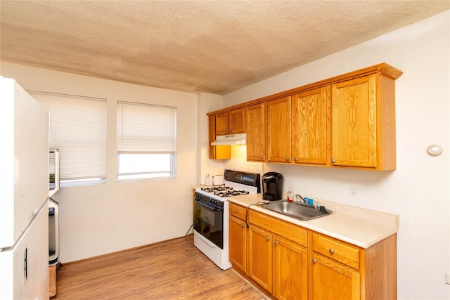 kitchen with under cabinet range hood, light countertops, white range with gas stovetop, light wood-style flooring, and a sink