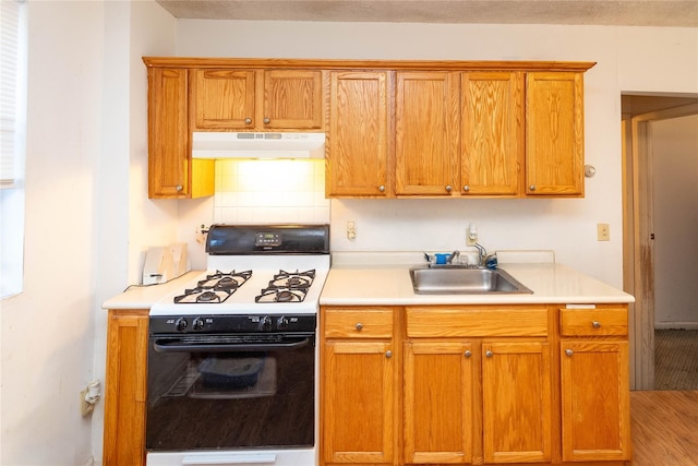 kitchen featuring gas stove, a sink, extractor fan, light countertops, and tasteful backsplash