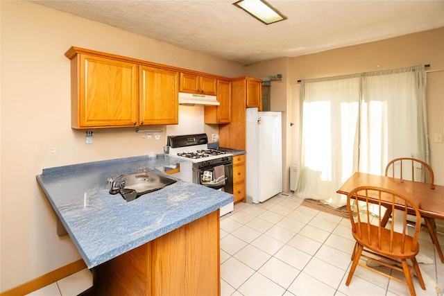 kitchen featuring brown cabinets, under cabinet range hood, freestanding refrigerator, range with gas cooktop, and a peninsula