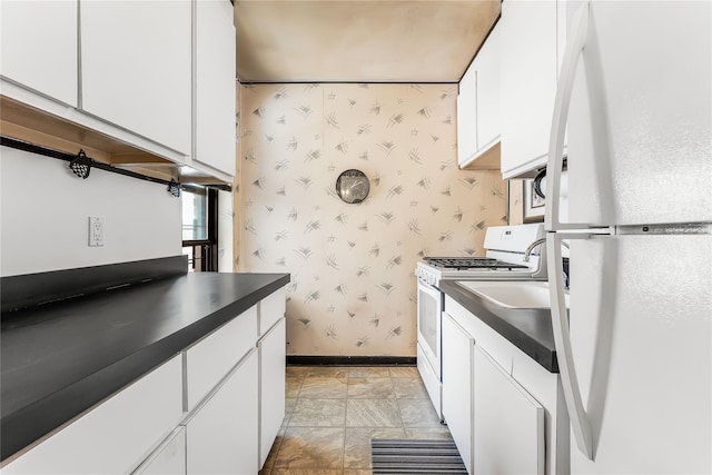 kitchen featuring white appliances, baseboards, white cabinets, dark countertops, and wallpapered walls