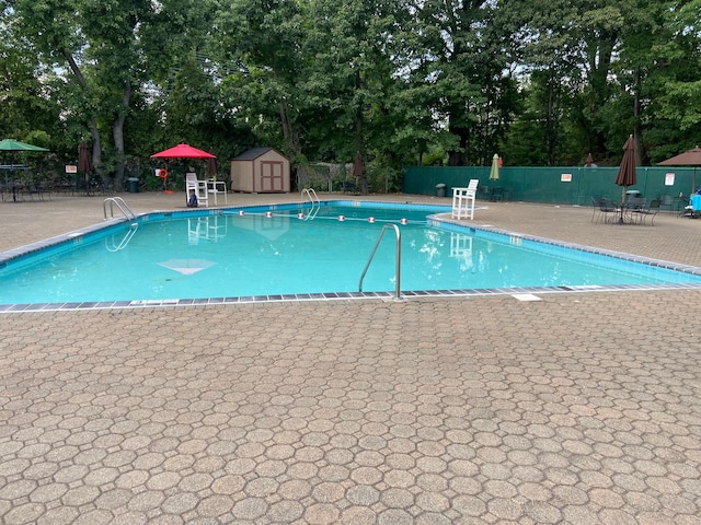 pool with a patio, a storage unit, an outdoor structure, and fence