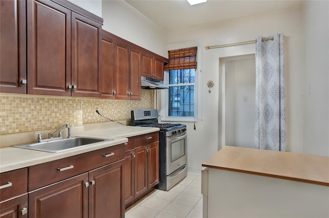 kitchen with under cabinet range hood, a sink, light countertops, decorative backsplash, and gas stove