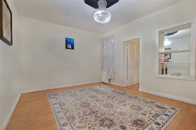 empty room featuring baseboards, wood finished floors, built in features, and radiator