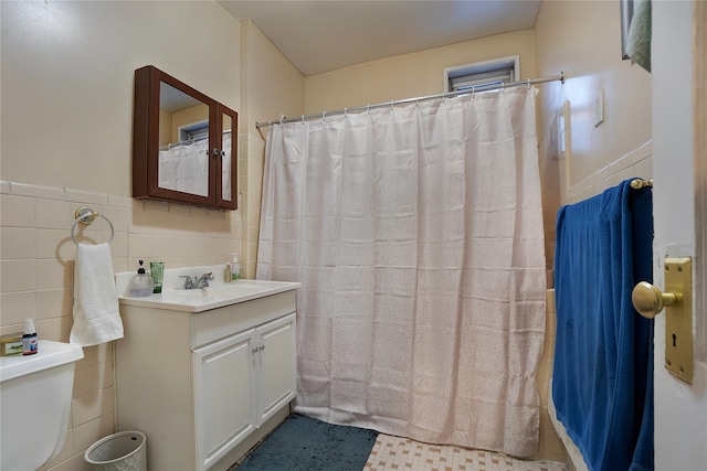 bathroom with toilet, wainscoting, vanity, and tile walls