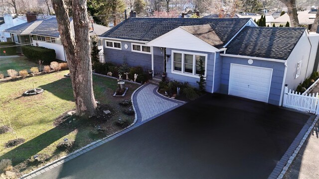 ranch-style home featuring fence, aphalt driveway, roof with shingles, a front yard, and an attached garage