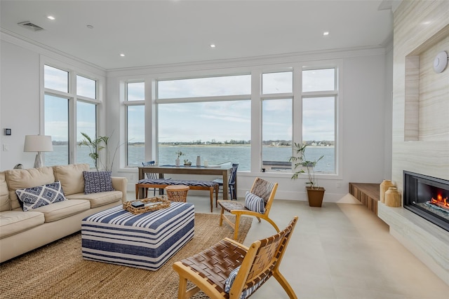 living area featuring a water view, visible vents, ornamental molding, plenty of natural light, and a glass covered fireplace