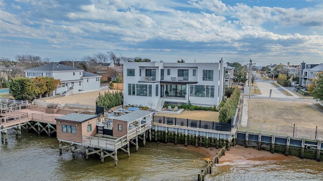 rear view of house featuring stucco siding, a water view, a balcony, and fence