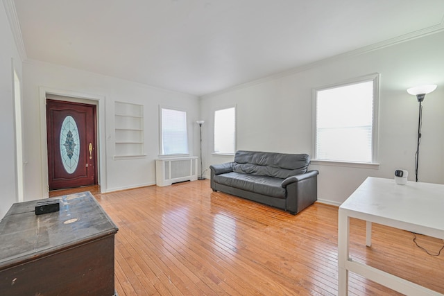 living room featuring baseboards, built in features, light wood-type flooring, radiator heating unit, and ornamental molding