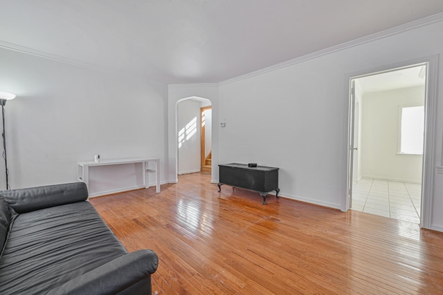 living area featuring stairway, arched walkways, crown molding, light wood finished floors, and baseboards