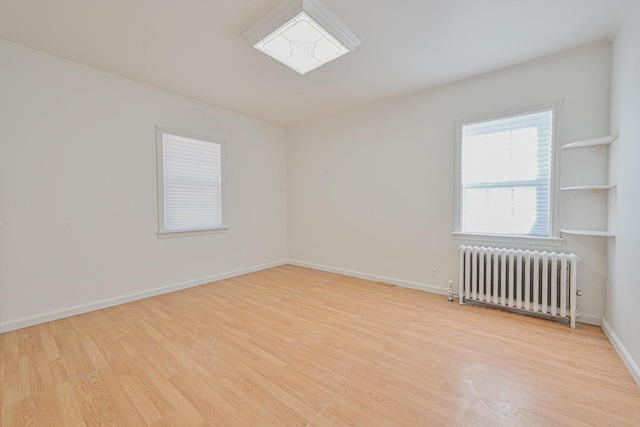 empty room with radiator heating unit, baseboards, and wood finished floors