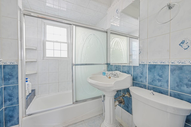 bathroom with combined bath / shower with glass door, toilet, tile walls, and tile patterned flooring