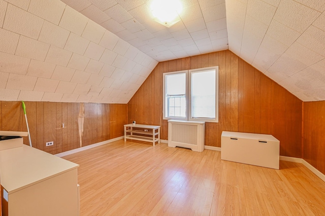 additional living space with lofted ceiling, radiator, and wood finished floors